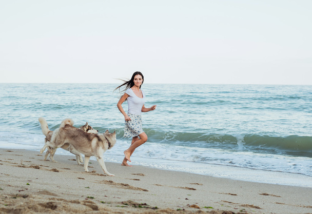 young caucasian female playing and having fun with siberian husky dog on beach - Foto, afbeelding