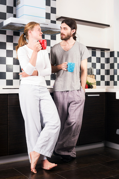 junge glücklich lächelnde kaukasische Pärchen in der Küche trinken Morgenkaffee und reden miteinander - Foto, Bild