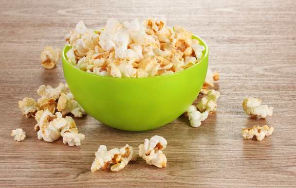 Popcorn in bright plastic bowl on wooden table - Фото, изображение