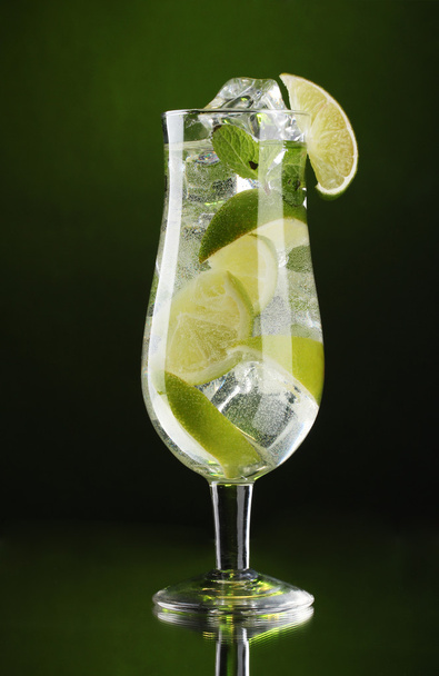 Glass of cocktail with lime and mint on green background - Фото, изображение