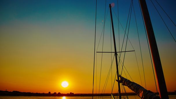 Purjevene liukuu meressä auringonlaskun aikaan
 - Valokuva, kuva