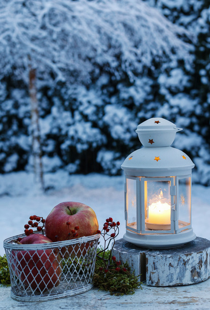 Winter evening in the garden. Iron lantern and basket of apples - Foto, afbeelding