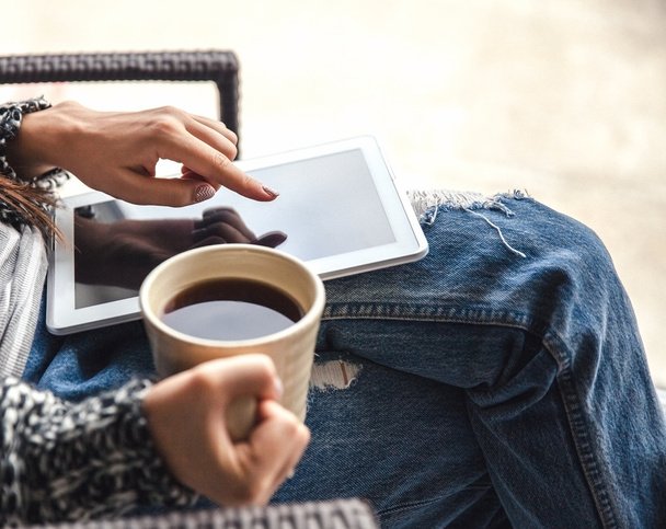 Foto macia da mulher Na poltrona com tablet e xícara de café nas mãos, jeans rasgados
 - Foto, Imagem
