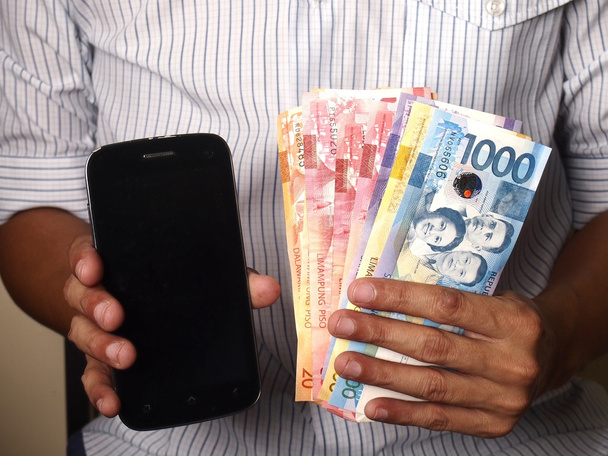 Man met een smartphone en Filippijnse peso rekeningen - Foto, afbeelding