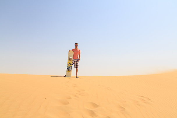 Young man standing on a dune with sand board - 写真・画像
