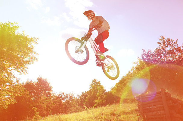 Спортсмен в спортивной одежде на горном велосипеде прыгает на трамплине
 - Фото, изображение