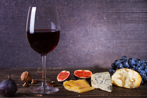 Glass of red wine, cheese, grape, walnuts, figs, plums and apple on wooden background - Fotó, kép