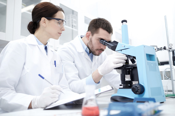Οι επιστήμονες με πρόχειρο και μικροσκόπιο στο εργαστήριο - Φωτογραφία, εικόνα