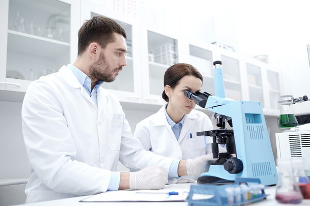 scientists with clipboard and microscope in lab - Photo, image