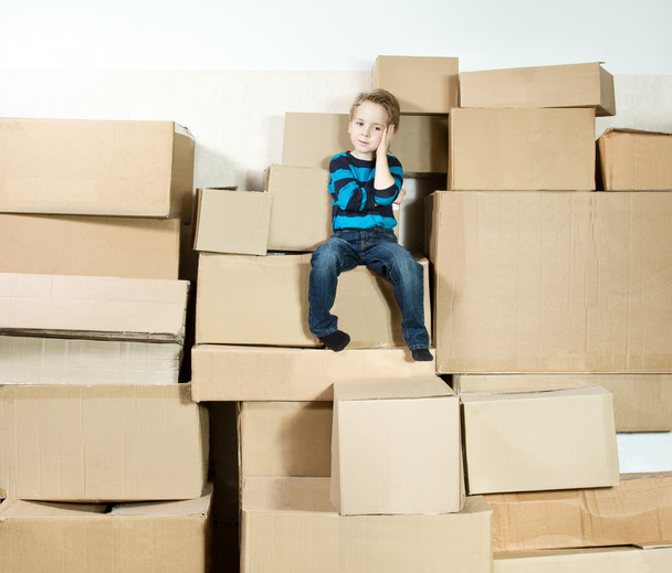 Child sitting on the top of stack packed boxes. - Фото, зображення