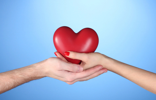 Man and woman holding red heart in hands on blue background - Foto, afbeelding