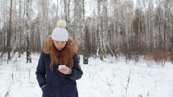 La chica caminando en el bosque de invierno con el teléfono
 - Metraje, vídeo