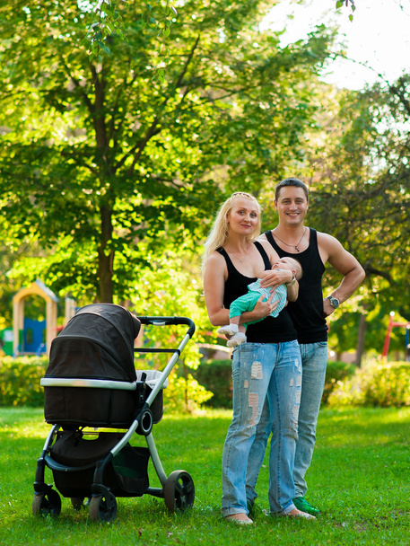 Des parents heureux debout près d'un landau dans le parc
 - Photo, image