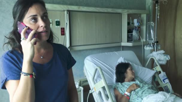 Kobieta mówi na jej telefon komórkowy obok kobiece leżący w szpitalnym łóżku - Materiał filmowy, wideo