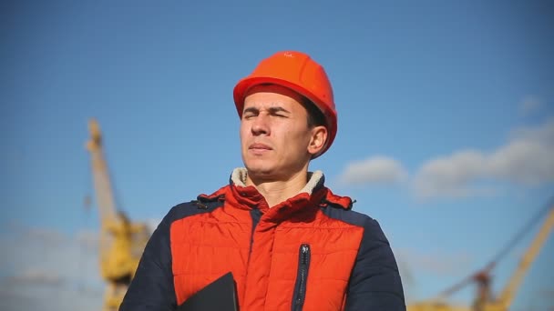 青い空と建設の背景にオレンジ色のヘルメットの男建設労働者の肖像 - 映像、動画