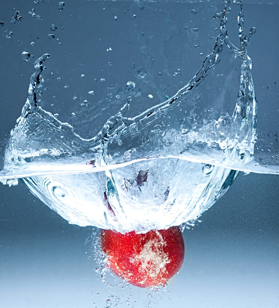 Красное яблоко брызгает в воду на голубом фоне
 - Фото, изображение
