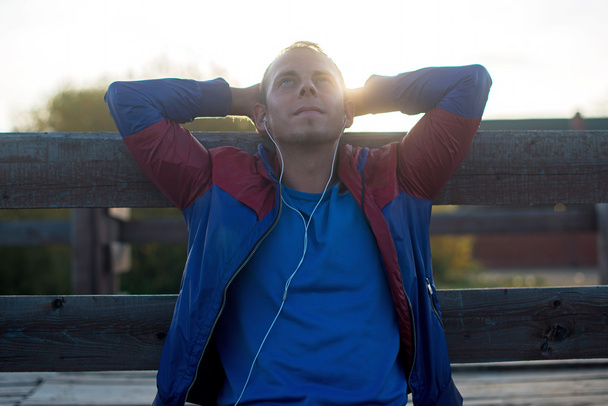 tired runner sitting, relaxing and listening to music  your phone, eyes closed on a wooden pier, sport. - Fotoğraf, Görsel