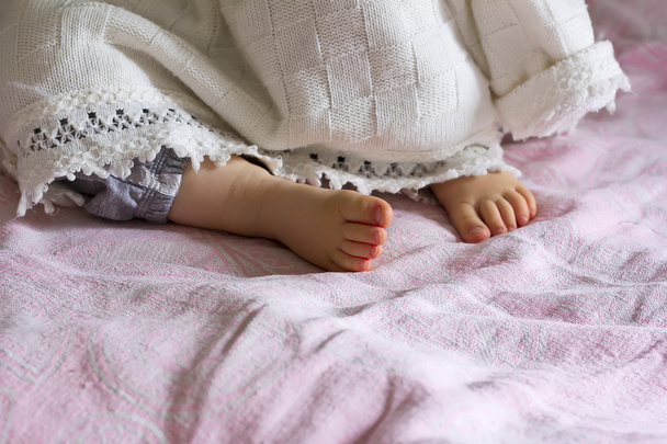 Heel sleeping baby girl sticking out from under the blanket, selective focus - Фото, изображение