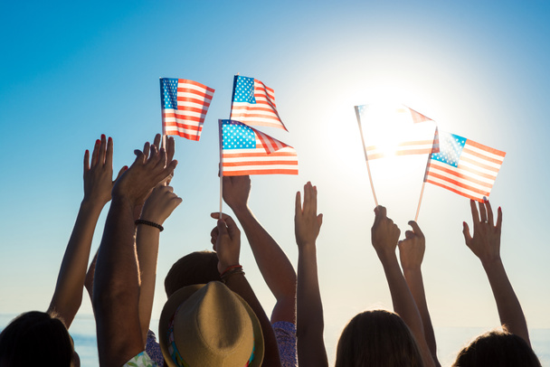 Νέοι άνθρωποι κουνώντας αμερικανικές σημαίες στο ηλιοβασίλεμα. - Φωτογραφία, εικόνα