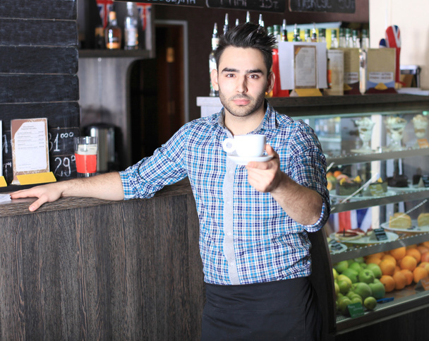 Handsome barista offering a cup of coffee to camera - Фото, изображение