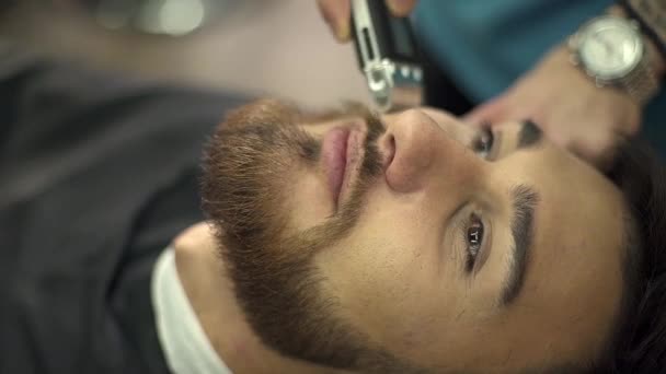 Close-up barber drying hair of a young bearded man - Felvétel, videó