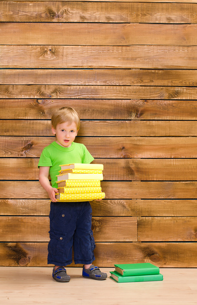 little boy with stack of books at wooden wall - Photo, Image