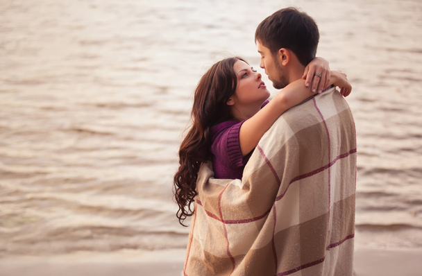 Couple in love on the shore wrapped in a plaid, cool evening. - Photo, Image