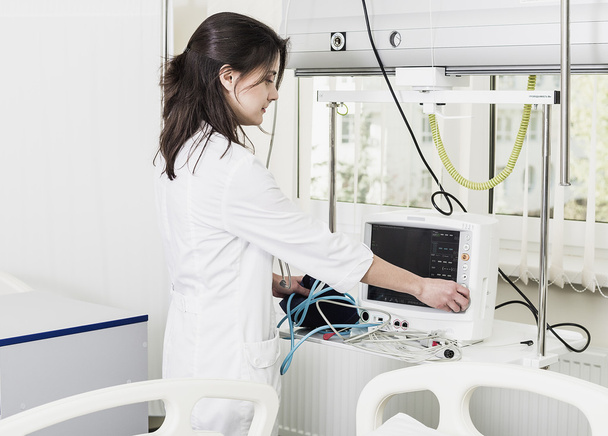 dziewczyna lekarz w biały płaszcz dostosowuje klinicznych urządzenia i monitor - Zdjęcie, obraz