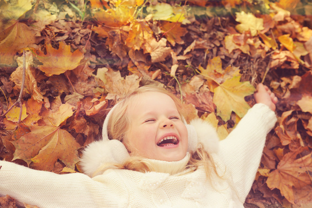 Little blonde girl portrait lying on autumn yellow maple leaves outstretched hands and smiling. - Photo, Image