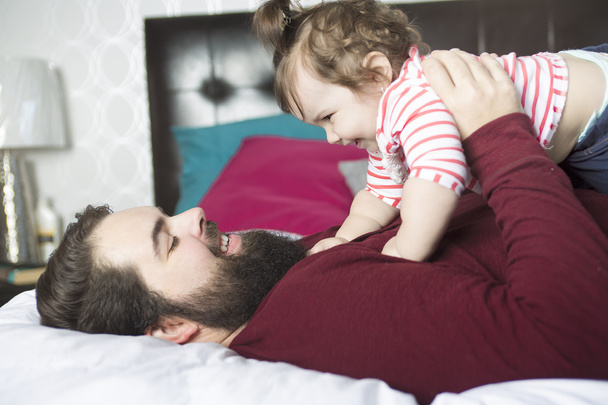 Портрет щасливого молодого батька з дитиною в ліжку вдома
 - Фото, зображення