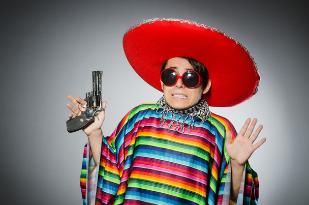 Mann im hellen mexikanischen Poncho hält Handfeuerwaffe gegen Grau - Foto, Bild