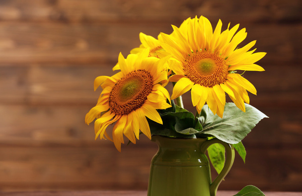 Beautiful bright sunflowers in pitcher on wooden background - 写真・画像