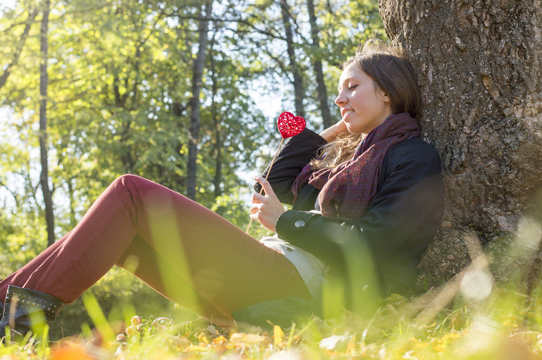 Mooi meisje rood hart op een stok te houden terwijl zittend op de - Foto, afbeelding