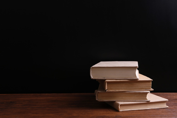 Pile de vieux livres fermés sur table en bois sur fond noir
 - Photo, image