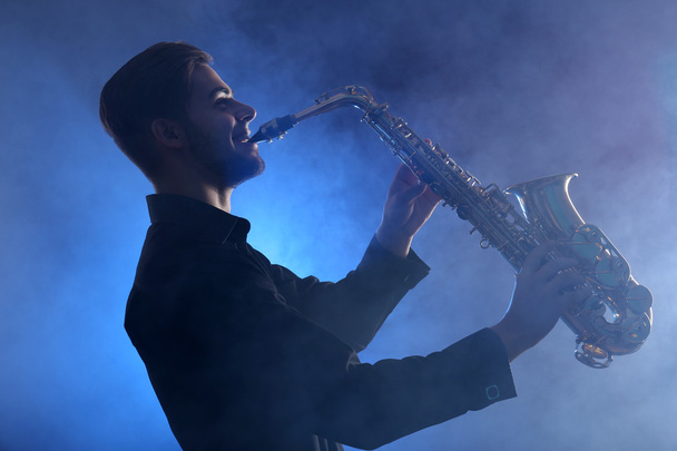 Elegant saxophonist plays jazz  in blue smoke - Foto, imagen