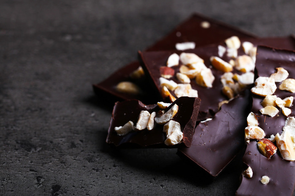Black chocolate pieces and nuts on dark gray background - Фото, изображение
