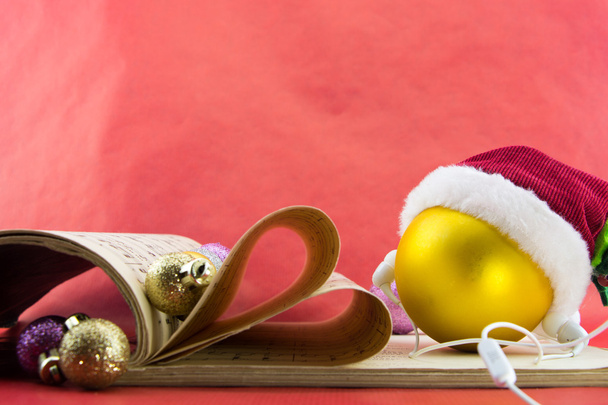 Boule de Noël avec chapeau et écouteurs du Père Noël, livre de notation musicale avec des pages façonnant le cœur, sur fond rouge
. - Photo, image