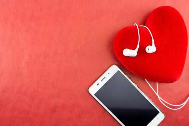 Corazón con smartphone y auriculares primer plano en rojo con espacio de copia
 - Foto, imagen