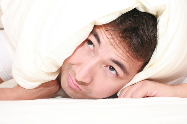 Homem tentando dormir com um travesseiro sobre a cabeça e perto de acordar
 - Foto, Imagem