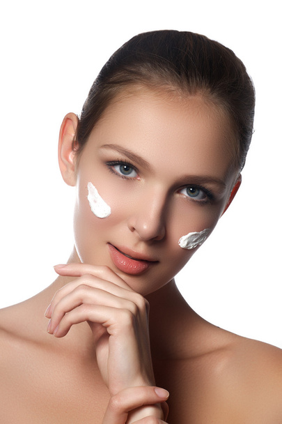 Skin care lady putting face cream. Attractive brunette girl on white background. Beautiful face of young woman with cosmetic cream on a cheek. Skin care concept. Skincare products - Foto, Imagen