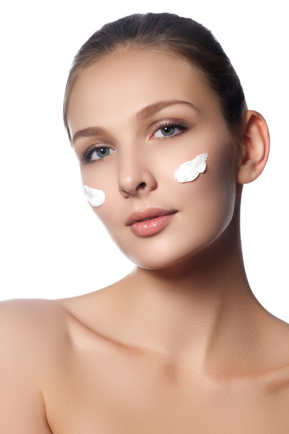 Beautiful face of young woman with cosmetic cream on a cheek. Skin care concept. Closeup portrait isolated on white. Close-up young beautiful face of girl applying moisturize cream - Foto, Imagen
