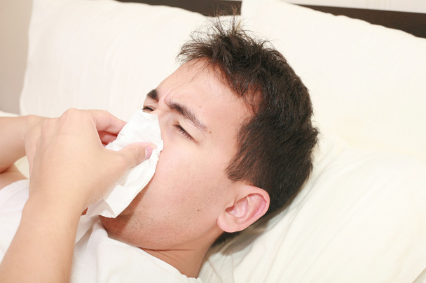 Homem doente soprando o nariz deitado em sua cama de manhã
 - Foto, Imagem