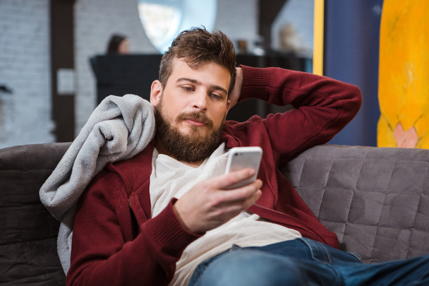 Relaxed young man lying on sofa and using cellphone - Foto, Imagem