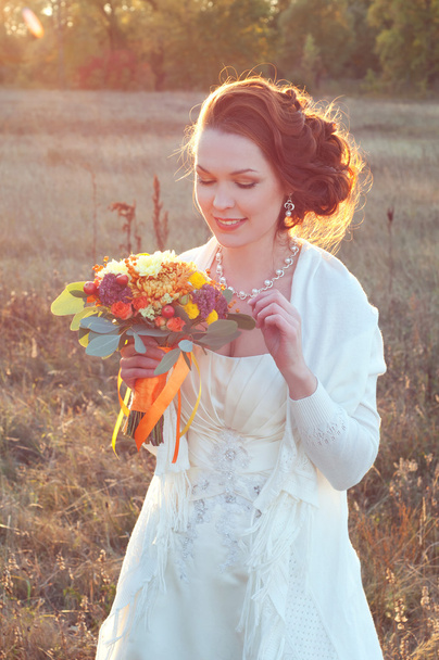 Beautiful redhead bride in white dress holding autumn bouquet - Photo, Image