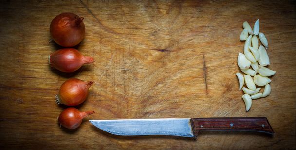 Hagymát, fokhagymát és a kést, egy rusztikus, fából készült asztal. - Fotó, kép