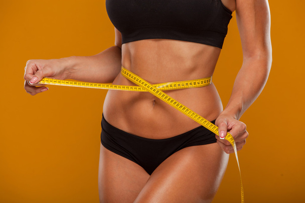 Sport, fitness and diet concept - close up of trained belly with measuring tape - Foto, Bild
