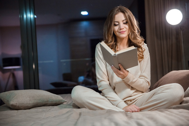 Beautiful young woman sitting on the bed and reading - Foto, immagini