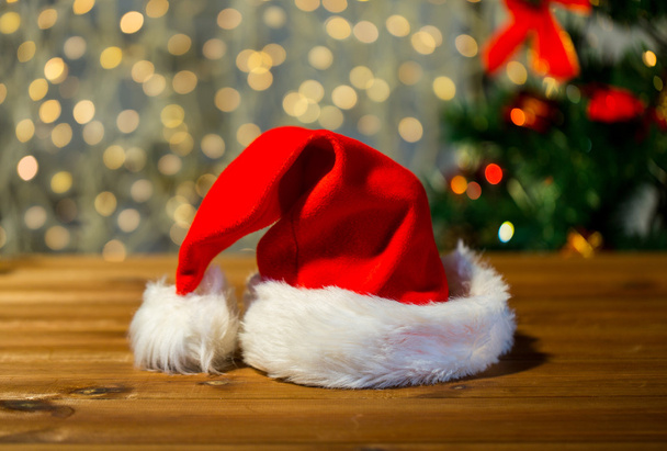 close up of santa hat on wooden table over lights - Φωτογραφία, εικόνα