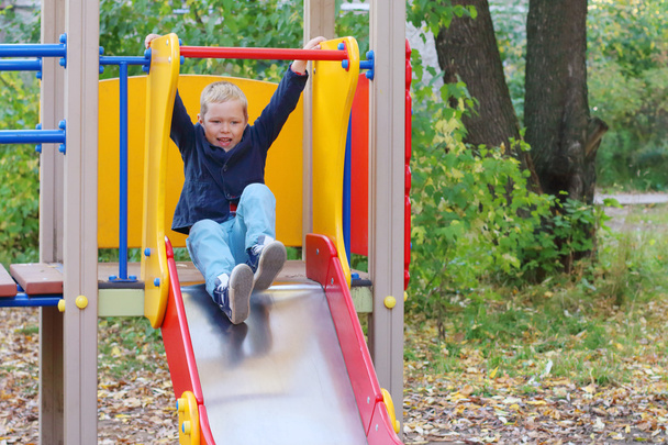 Handsome little boy plays on slide on playground in autumn day - Foto, afbeelding