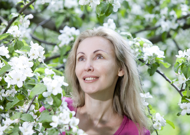 Молодая привлекательная женщина стоит рядом с цветущей яблоней
 - Фото, изображение